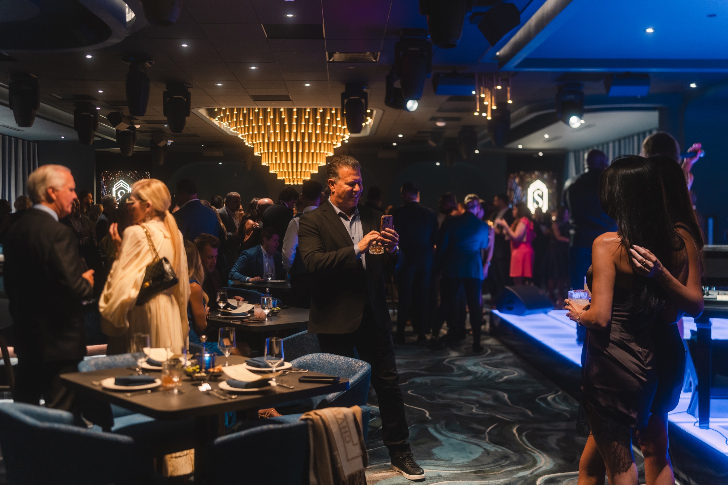 Guests gathering in an upscale event room beneath a gold chandelier