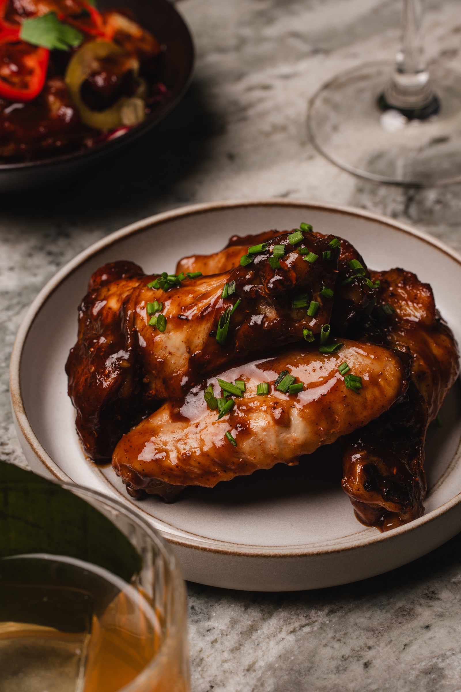 Glazed chicken wings served on stoneware beside drinks