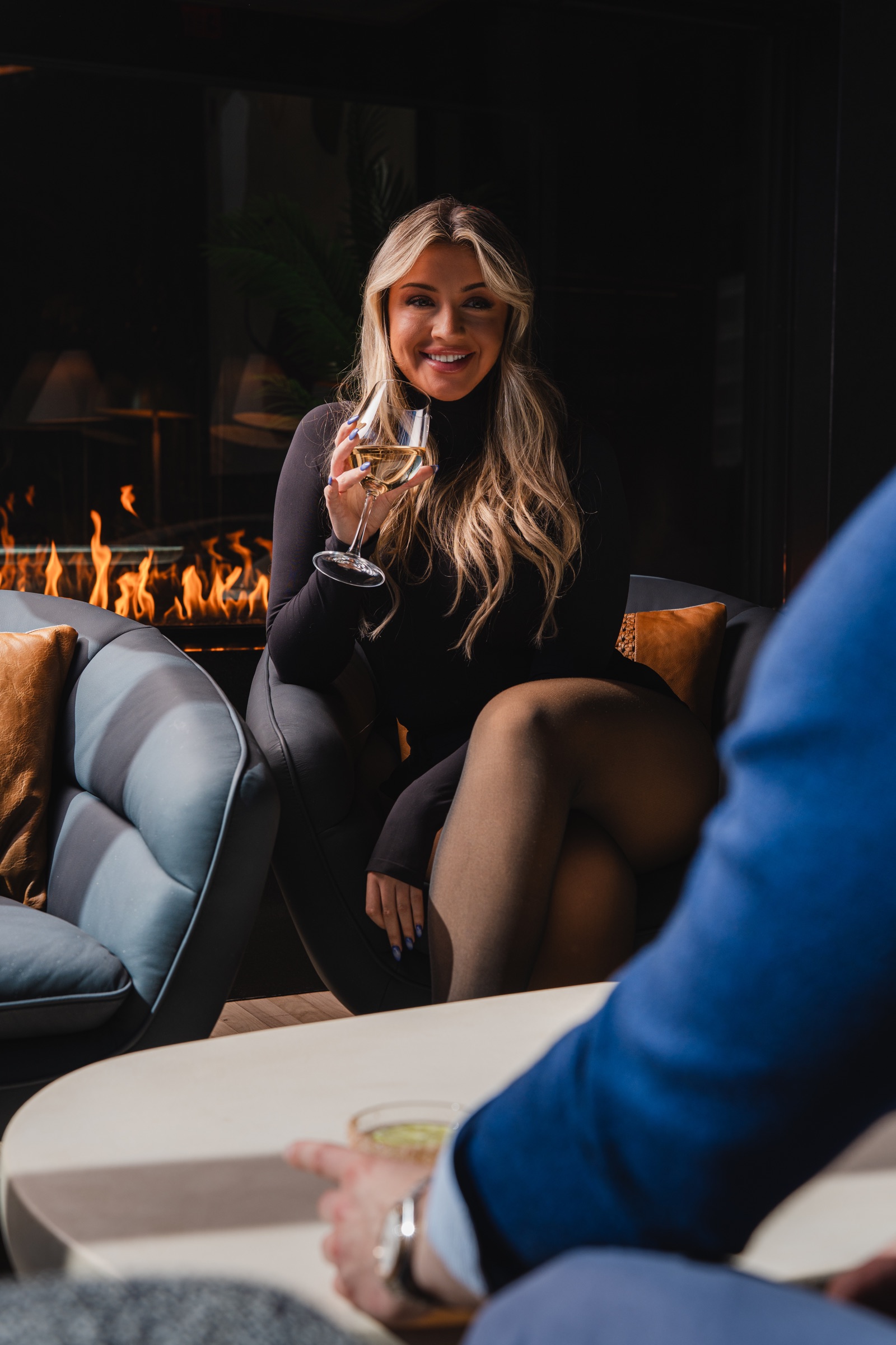Guest enjoying wine beside a fireplace in an intimate lounge