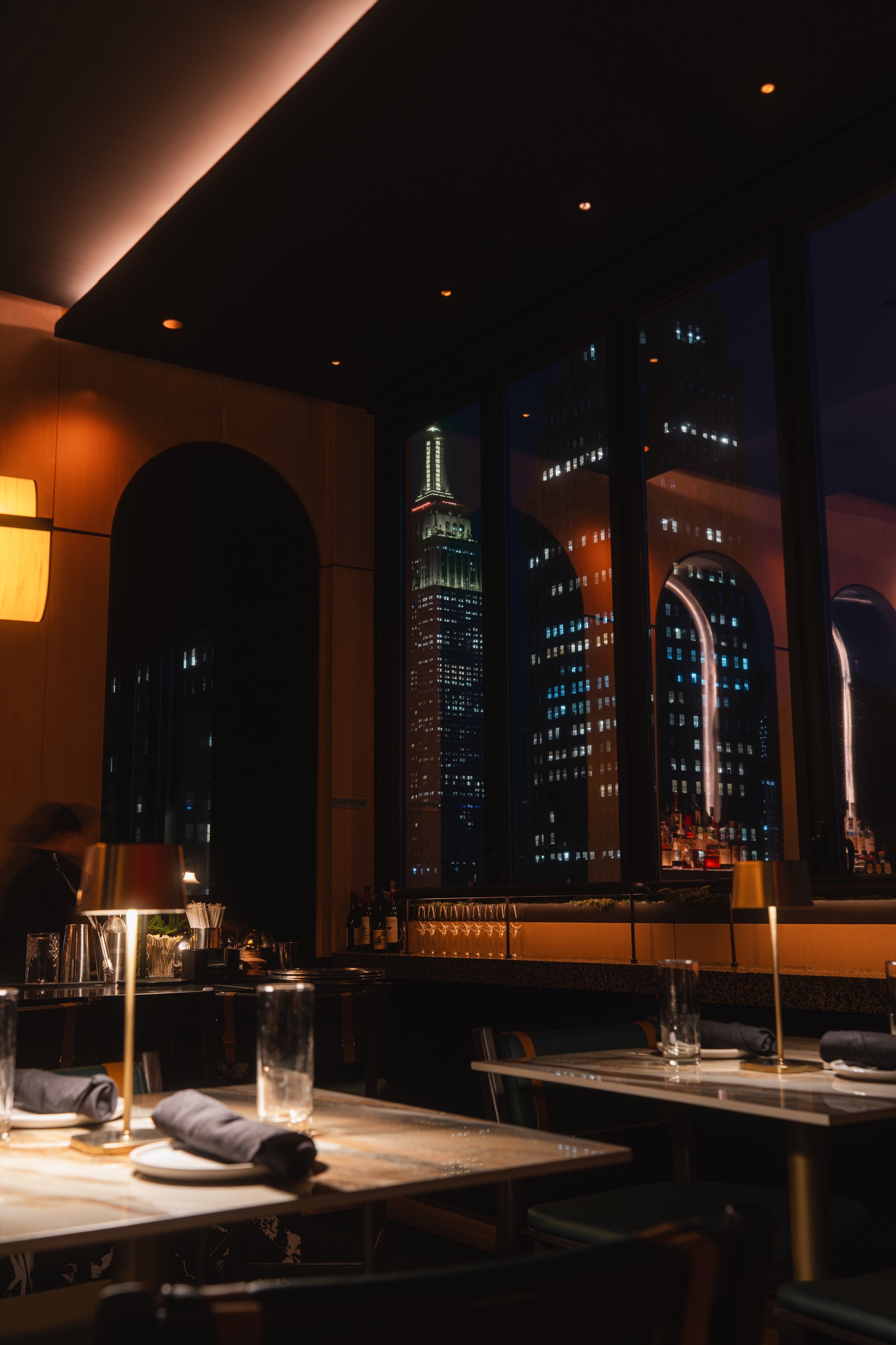 Warm restaurant interior overlooking the Empire State Building at night