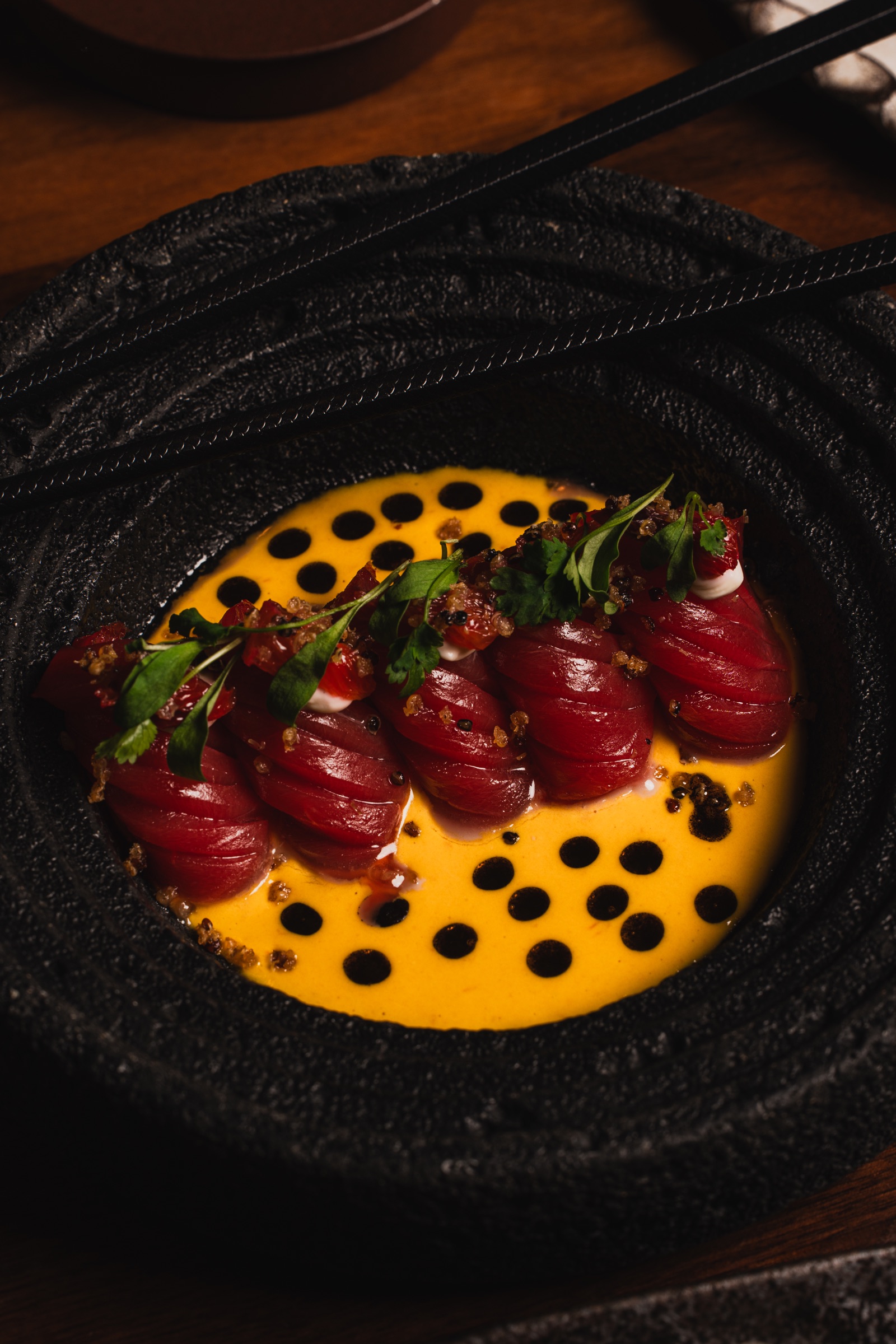 Sliced tuna presented over a vivid yellow sauce on black ceramic